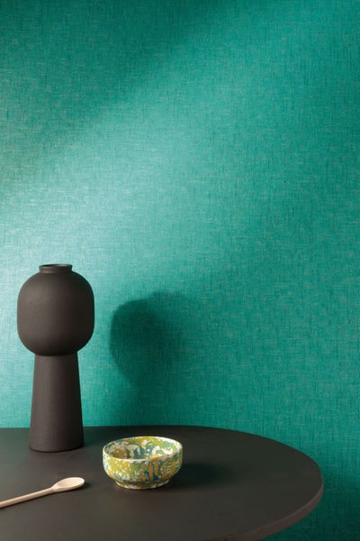 Nahaufnahme einer grünen Textiltapete mit einer Vase, einer Schale und einem Löffel auf einem Tisch.