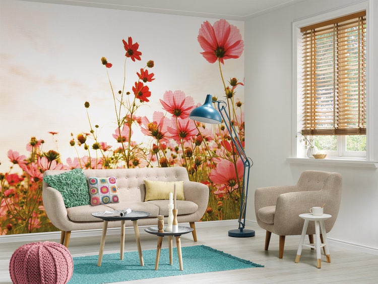 Fototapete mit Blumenwiese aus rosa und roten Kosmeen in einem hellen, modern eingerichteten Wohnzimmer mit beigem Sofa und blauem Teppich.