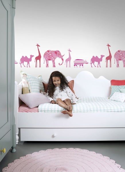 Mädchen sitzt auf einem Kinderbett mit Tier Wandtattoo im Hintergrund