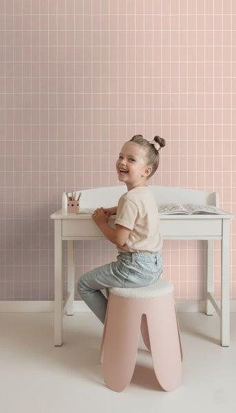 Kind sitzt an einem Schreibtisch vor einer Wand mit Fliesenmuster