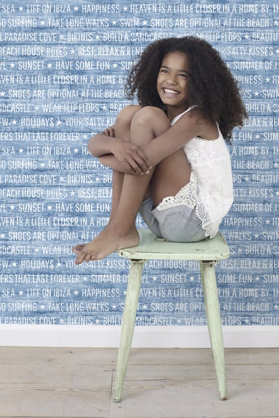 Mädchen sitzt auf einem Hocker vor einer mit Schrift bedruckten Tapete