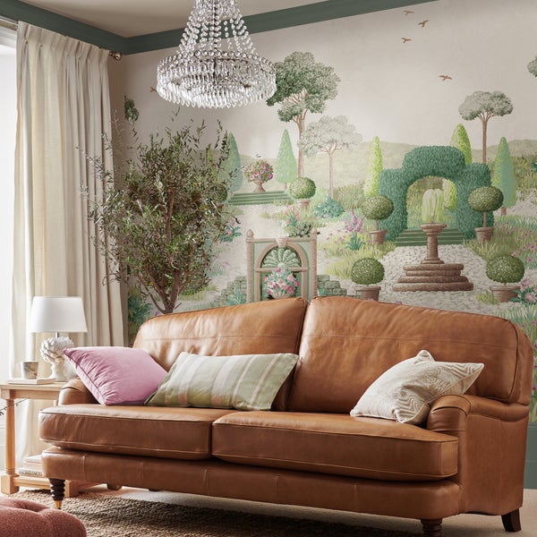 Wohnzimmer mit braunem Ledersofa und einer Wandtapete mit einer Gartenlandschaft und einem Brunnen.