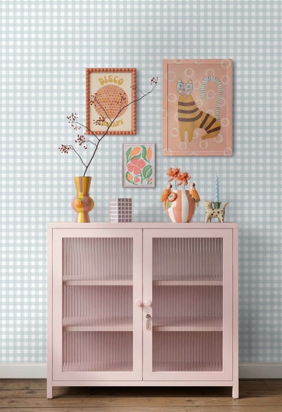 Vliestapete mit blau-weißem Karo-Muster hinter einem hellrosa Metallschrank mit Glastüren und bunter Dekoration.