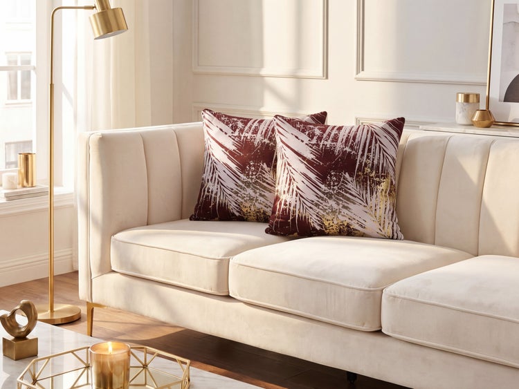Zwei Dekokissen mit Palmblatt-Muster auf einem cremefarbenen Sofa in einem hellen, modern eingerichteten Wohnzimmer mit goldener Stehlampe.