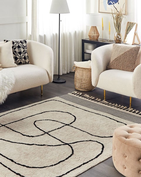 Modernes Wohnzimmer mit beigefarbenem Teppich mit abstraktem schwarzem Linienmuster, cremefarbenen Bouclé-Sesseln und einem Hocker.