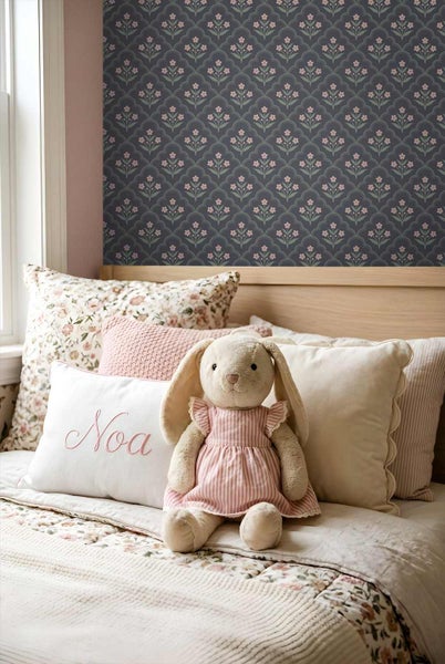 Gemütliches Kinderzimmer mit einer gemusterten Tapete mit Blumenmotiven. Auf dem Bett liegen verschiedene Zierkissen und ein Stoffhase.
