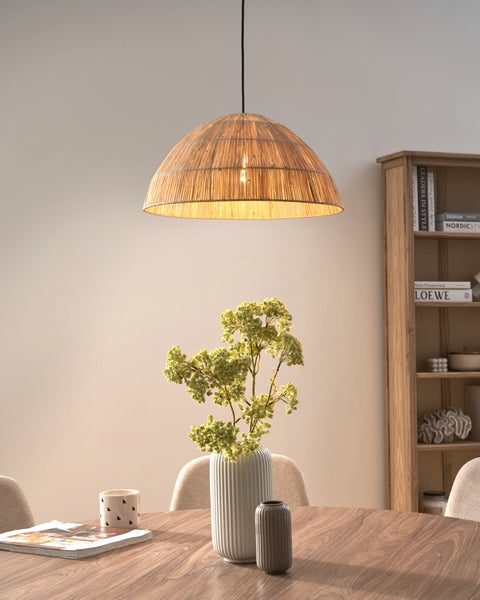 Pendelleuchte in Kuppelform aus Naturgeflecht über einem runden Holztisch mit Vase und Pflanzen in einem hellen, organisierten Raum mit Bücherregal.