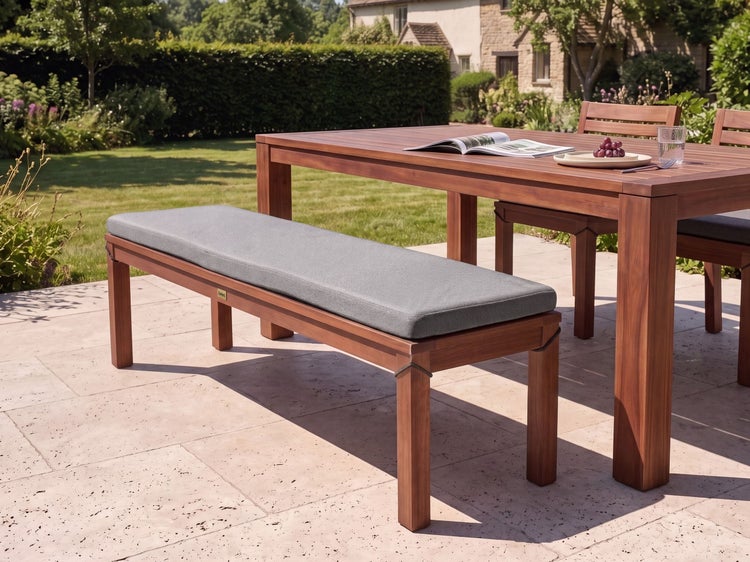 Gartenbank aus Holz mit einem weichen Sitzpolster auf einer Terrasse im Garten neben einem passenden Gartentisch.