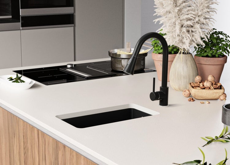 Küchenszene mit Spüle, Armatur, Kochfeld und dekorativen Elementen auf einer hellen Arbeitsplatte