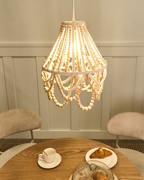 Hängelampe mit Holzperlen über einem Holztisch mit Croissants und einer Tasse