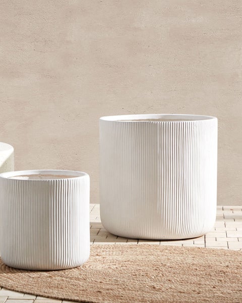 Zwei weiße, gerippte Pflanzgefäße unterschiedlicher Größe stehen auf einem Teppich.