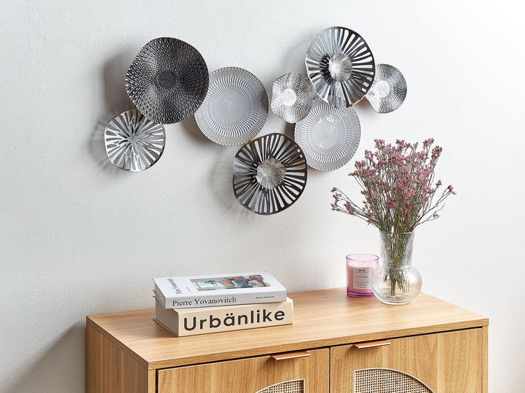 Dekorative Wandobjekte in Tellerform aus Metall über einem Sideboard mit Dekorationsgegenständen.