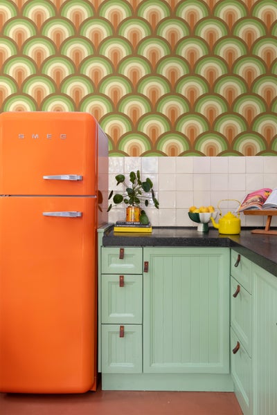 Küchenszene mit orangefarbenem Smeg Kühlschrank, grünen Schränken und Retro-Tapete