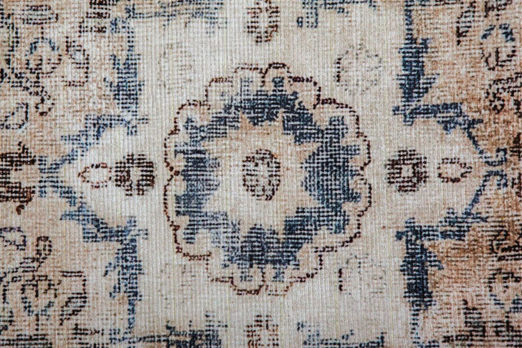Nahaufnahme eines Teppichs in Beige, Blau und Braun mit Vintage-Muster, floralen und geometrischen Elementen, gewebte Textur.