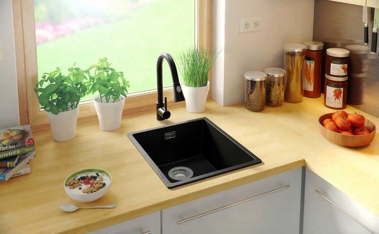 Küchenszene mit Spüle, Armatur, Lebensmitteln und Küchenutensilien auf einer hellen Arbeitsplatte