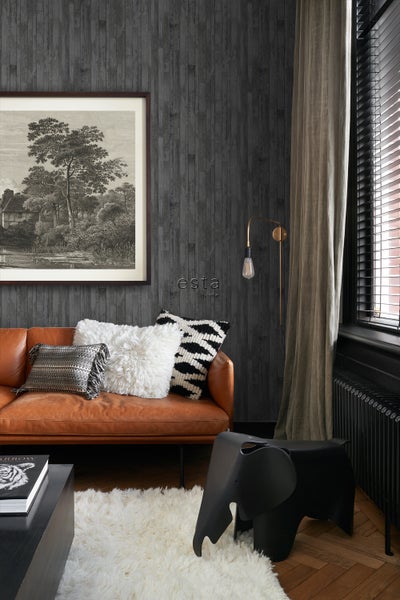 Wohnzimmer mit braunem Ledersofa, Kissen und schwarzem Elefantenhocker vor einer grauen Holzwand