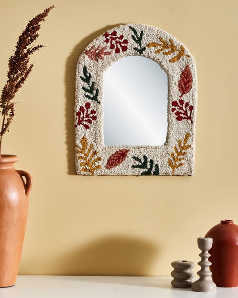 Dekorativer Spiegel mit Blattmusterrahmen und keramische Dekorationsgegenstände auf einem Tisch.