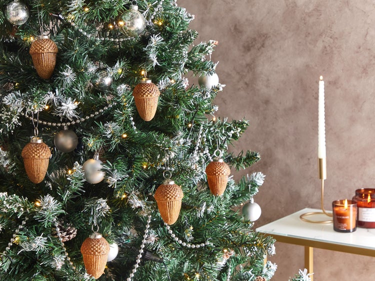 Geschmückter Weihnachtsbaum mit Tannenzapfen-Anhängern und Christbaumkugeln neben einer Kerze
