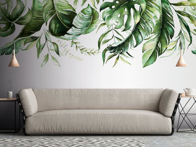 Fototapete mit tropischen Blättern im Aquarellstil über einem Sofa in einem hellen, modern gestalteten Wohnzimmer.