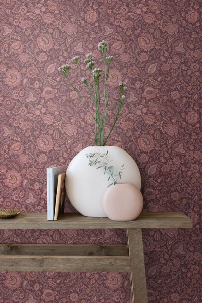 Helles Esszimmer mit floral gemusterter Vliestapete, einem Kaminofen, einem Holztisch und einem Fenster mit Blick in den Garten.