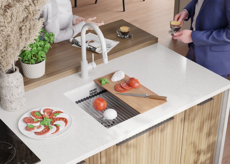Küchenszene mit Spüle, Armatur, Schneidebrett, Tomaten, Mozzarella, Basilikum und Geschirr