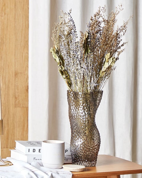 Dekorative Trockenblumen in einer bauchigen Glasvase auf einem Tisch.