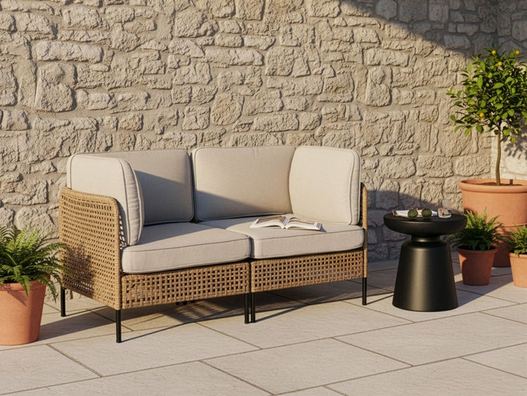 Gartenszene mit Korbsessel, Beistelltisch und Topfpflanzen vor einer Steinwand