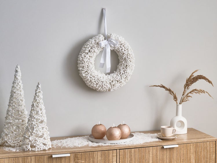 Dekoratives Arrangement mit einem Kranz, Bäumen, Kerzen und einer Vase auf einem Sideboard.