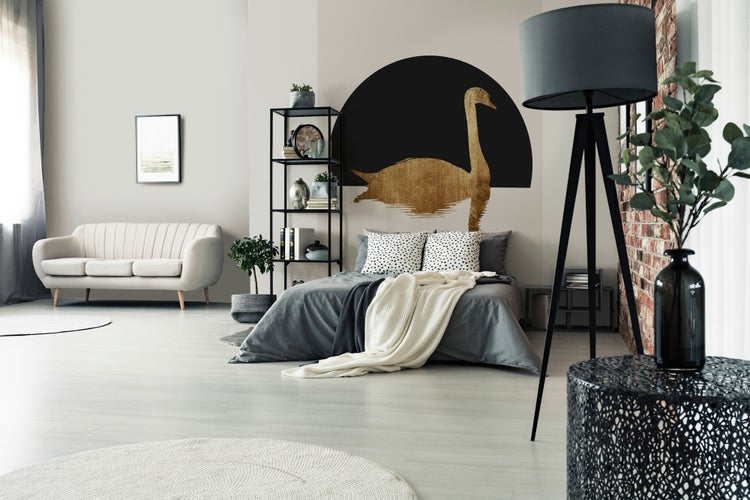Modernes Schlafzimmer mit Bett, goldener Schwan Wanddekoration, schwarzem Metallregal, Stativ-Stehlampe, Sofa und hellem Teppich.