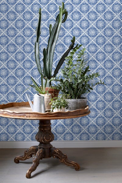 Dekoratives Arrangement mit Zimmerpflanzen auf einem Holztisch vor einer gemusterten Tapete.