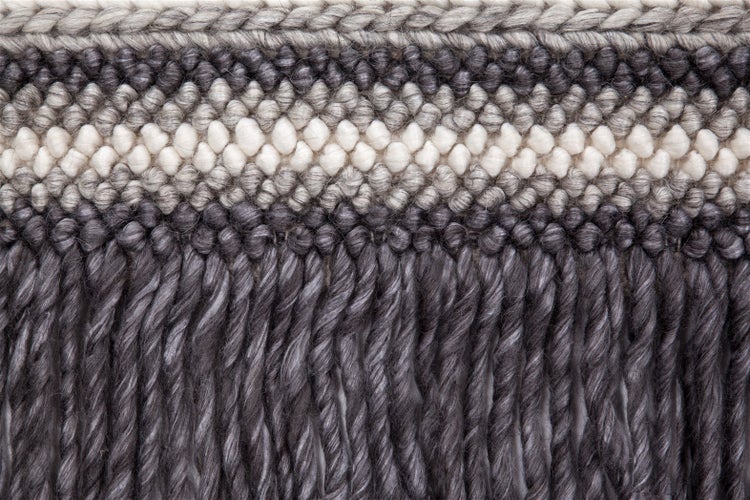 Detailaufnahme eines handgewebten Teppichs mit Noppenstruktur und langen Fransen.