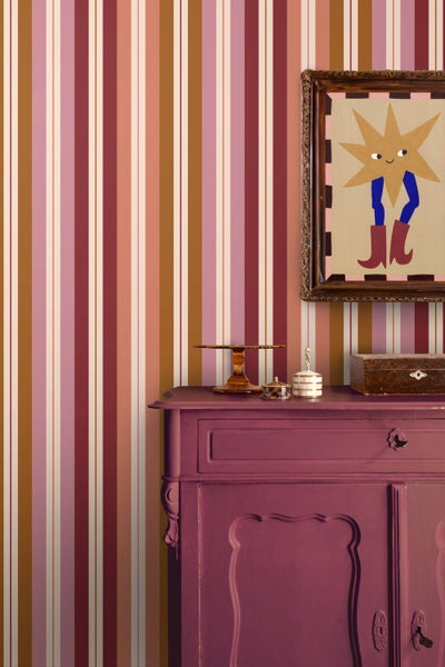 Vliestapete mit vertikalem Streifenmuster in einem Wohnraum hinter einer Kommode mit Dekoration und einem gerahmten Bild.