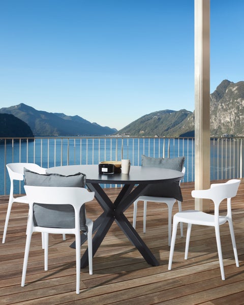 Runder Gartentisch mit vier Stühlen und Kissen auf einer Terrasse mit Seeblick