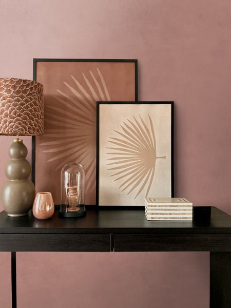 Dekorative Szene mit Tischleuchte, Bilderrahmen und Dekorationsartikeln auf einem dunklen Tisch.