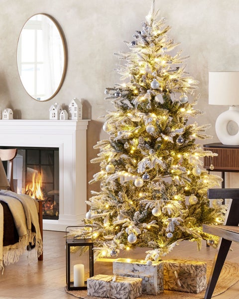 Dekorierter Weihnachtsbaum mit Lichtern und Geschenken in einem Wohnzimmer mit Kamin