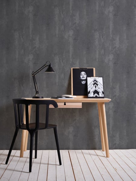 Schreibtisch mit Stuhl, Lampe und Dekoration auf hellem Holzboden vor grauer Wand