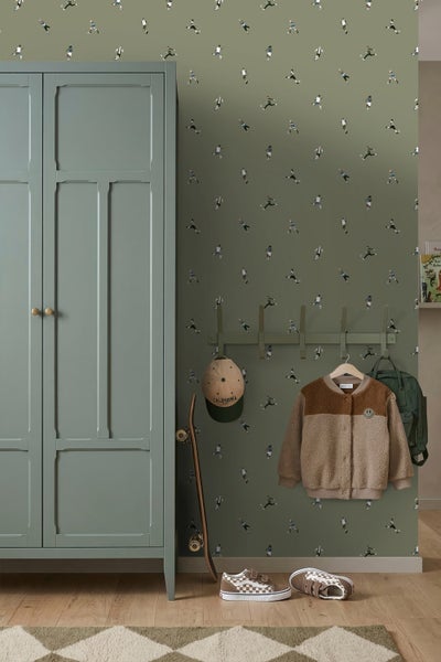 Kinderzimmer mit grüner Fußball-Tapete, Kleiderschrank, Garderobenleiste mit Jacke, Skateboard und Schuhen auf Holzboden.