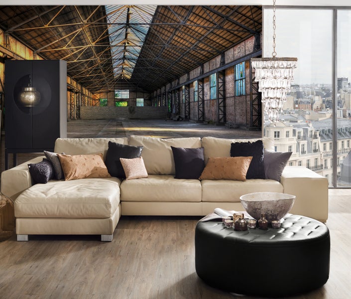 Fototapete einer leeren Industriehalle als Wandgestaltung in einem modernen Wohnzimmer mit hellem Ledersofa.