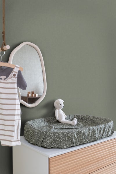 Ein Wickeltisch mit Wickelauflage, einem Spiegel und einem Stofftier in einem Kinderzimmer.