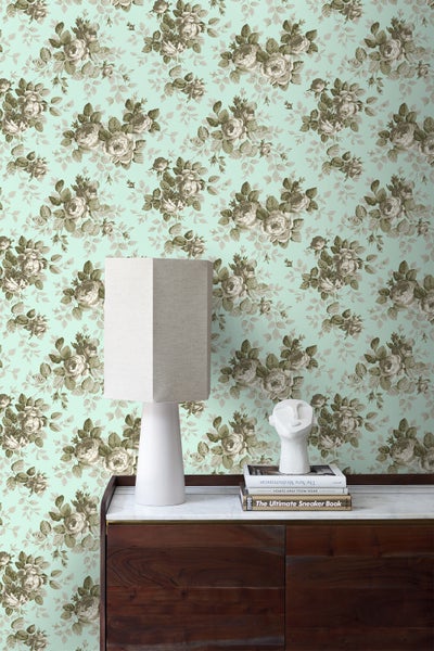 Wand mit floral gemusterter Tapete, Nachttischlampe und Dekorationsgegenständen.