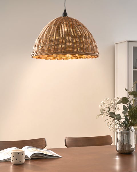 Rattan-Pendelleuchte über einem Holztisch mit Stühlen, einer Vase und einem Magazin in einem hellen Raum.
