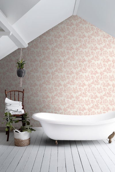 Badezimmer mit weißer freistehender Badewanne, Toile-de-Jouy-Tapete, Holzstuhl mit Handtüchern und Zimmerpflanzen auf hellem Dielenboden.