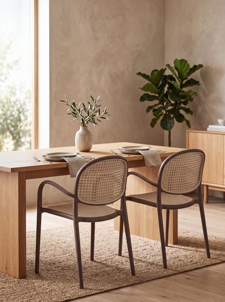 Ein heller, moderner Essbereich mit einem Holztisch und zwei Armlehnstühlen mit Geflechtoptik, ergänzt durch einen Teppich und eine Topfpflanze.