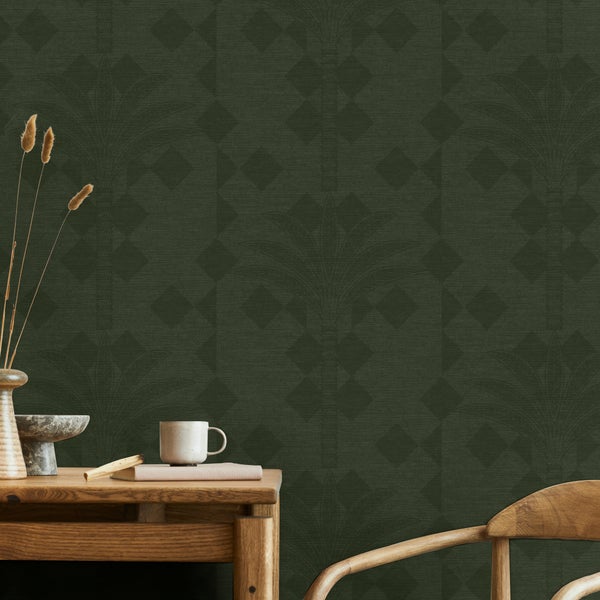 Dunkelgrüne Tapete mit geometrischem Muster und Palmenblättern an einer Wand hinter einem Holztisch mit Dekoartikeln und einem Holzstuhl.