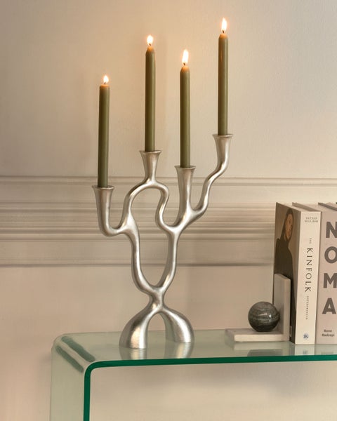 Silberfarbener Kerzenständer mit vier grünen Kerzen auf einem Glastisch neben Büchern