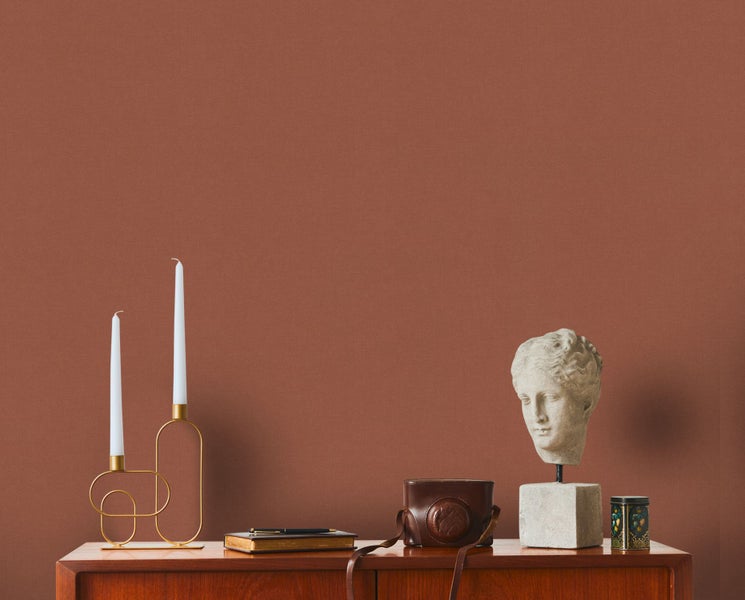 Dekoratives Stillleben mit Kerzen, Büchern und einer Büste auf einem Holzschrank vor einer Wand