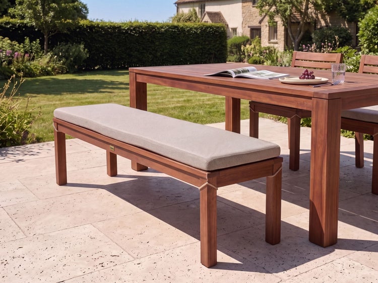 Gartenbank aus Holz mit einem beigen Sitzpolster auf einer Terrasse im Garten neben einem passenden Gartentisch.