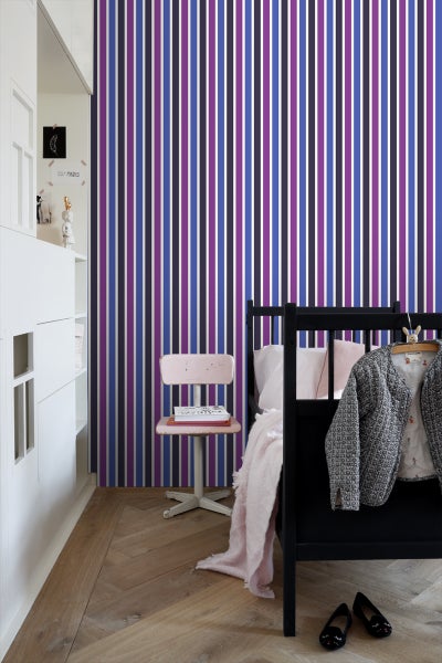 Ein Kinderzimmer mit einer Tapete mit vertikalen Streifen, einem Bett und einem Stuhl.