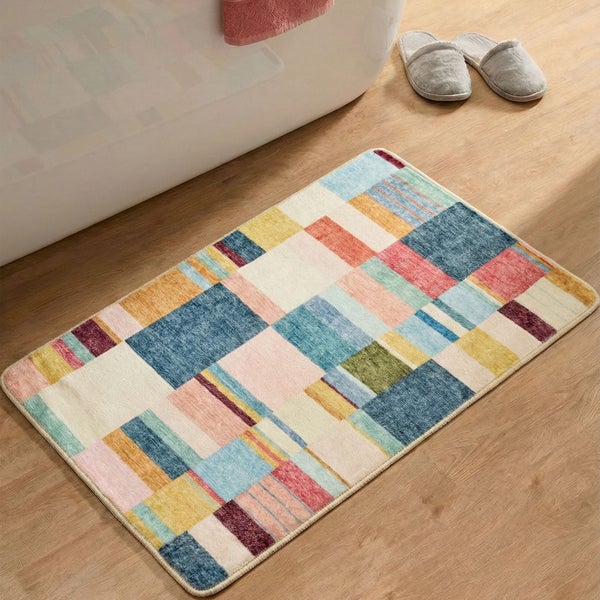 Badematte mit buntem geometrischem Karomuster auf Holzboden vor einer weißen Badewanne mit Hausschuhen.