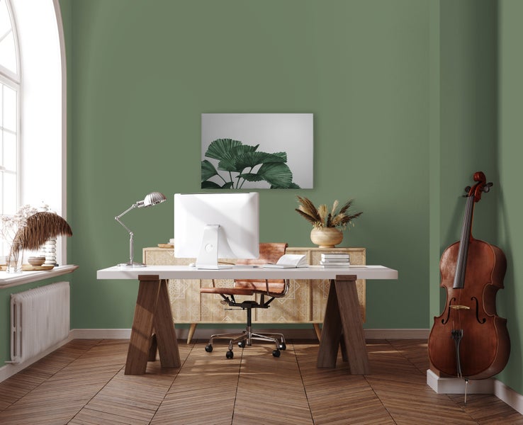 Ein modern eingerichtetes Arbeitszimmer mit einem Schreibtisch, einem Computer, einem braunen Bürostuhl und einem Kontrabass vor einer grünen Wand.